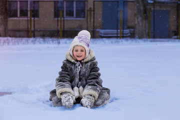 Fototapeta na wymiar A cute little girl covered with snow has fun in winter park, wintertime