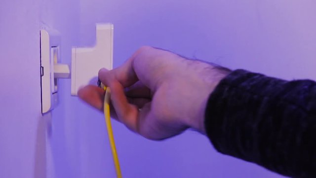 Man insert WiFi repeater into electrical socket on the wall and plug in a ethernet cable into it