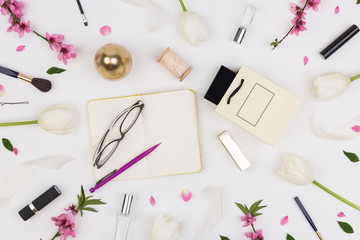 Fototapeta na wymiar femininity, organisation, lifestyle concept. among white tulips and brunches of oriental cherry there are different cosmetics stuff and glasses with daily planner