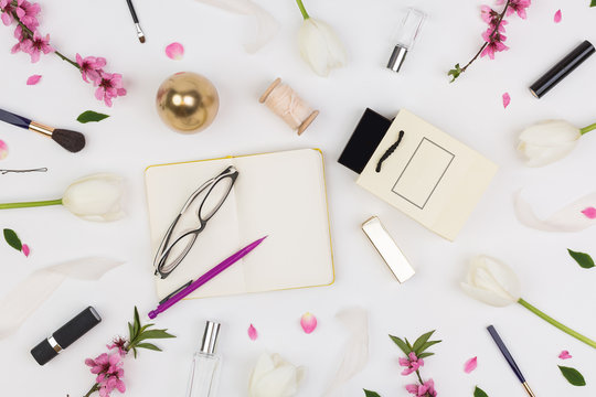 femininity, organisation, lifestyle concept. among white tulips and brunches of oriental cherry there are different cosmetics stuff and glasses with daily planner