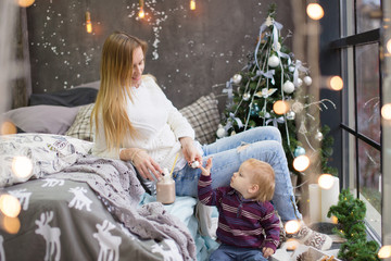 Portrait of a mother and child sitting in Christmas decorations, decorated Christmas tree outside