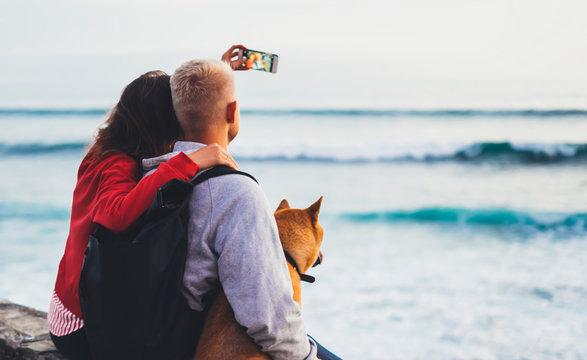 Couple hugging on background beach ocean sunrise, photos on mobile smartphone, two romantic people cuddling and looking on view evening seascape, travel holidays vacation, love relax concept
