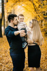 young family and newborn son posing for the camera in autumn park