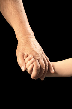 Hands of elderly man and baby on dark background