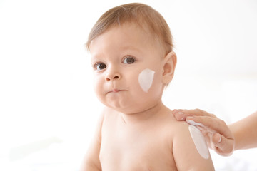 Woman applying body cream on her baby against light background