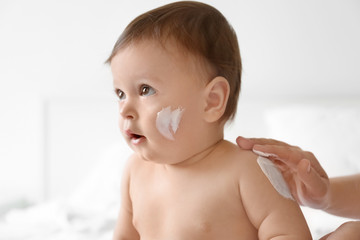 Woman applying body cream on her baby against light background