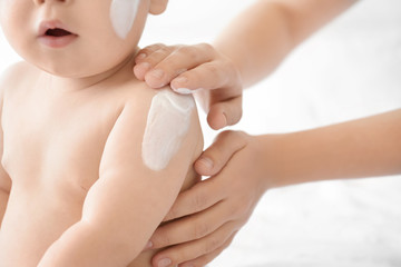 Woman applying body cream on her baby against light background