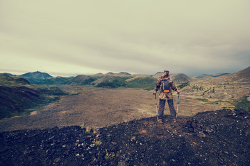 Fototapeta premium Lady hiker with backpack standing on top of the mountain, view from volcano peak to frozen lava valley
