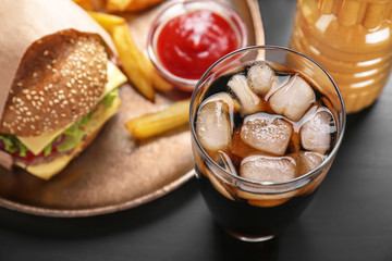 Glass of cold cola with tasty burger on table