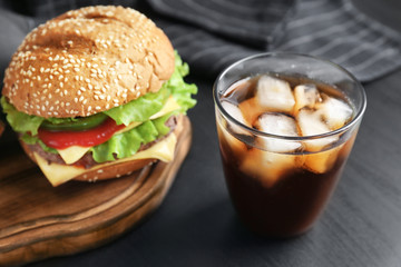 Glass of cold cola with tasty burger on table