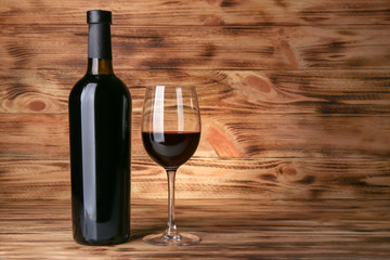 Bottle and glass with red wine on wooden background