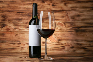 Glass of red wine and bottle with blank label on wooden background. Mock up for design