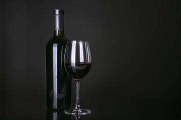 Bottle and glass with red wine on black background