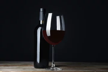 Fotobehang Bottle and glass with red wine on table against black background © Africa Studio