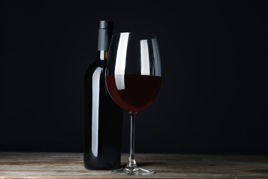 Bottle and glass with red wine on table against black background