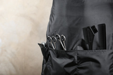 Person in black apron with professional hairdresser set on light background, closeup