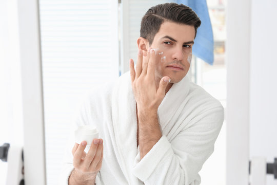 Handsome man applying face cream in bathroom