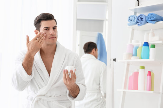 Handsome man applying face cream in bathroom