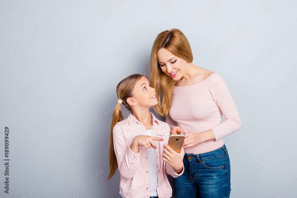 Wall mural Attractive, nice, cute kid indicate with index finger on digital smart phone screen to her lovely mother, showing something interesting, together doing online shopping