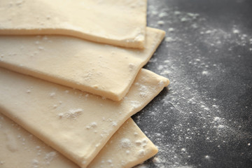 Raw flaky dough with flour on table