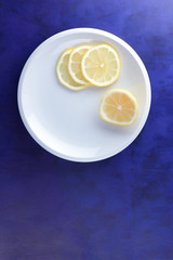 Sliced lemons on an ultraviolet background, fresh lemons on a white plate for vegan, vitamins, citrus in minimalism style, pop art, dark blue background with fruits