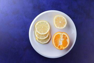 Sliced lemons on an ultraviolet background, fresh lemons on a white plate for vegan, vitamins, citrus in minimalism style, pop art, dark blue background with fruits