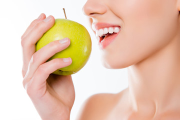 Vegetarian vitality wellbeing wellness concept. Cropped close up photo of white clean clear healthy woman's teeth trying to bite hard juicy green tasty apple in hand isolated on white background