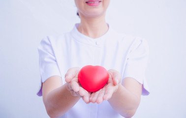 A nurse holding red heart toy. She is Left / right hand holding it. She is smile and good mood. The photo shows the principle of caring and good health.