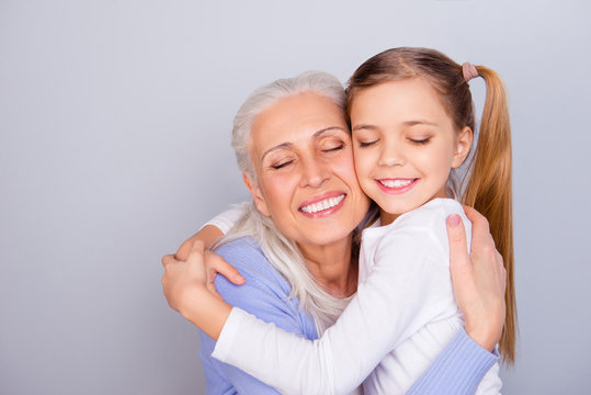 Close up portrait of adorable small lovely sweet charming beautiful girl hugging her careful attentive with white hair granny wearing casual clothes isolated on gray background