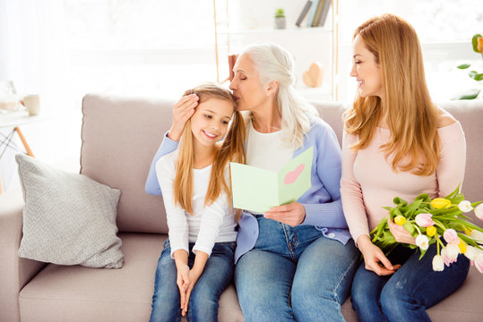 Motherhood parenthood relationship comfort people holiday festive concept. Cute friendly family gathering on birthday excited granny kissing sweet girl's head mommy with fresh beautiful flowers