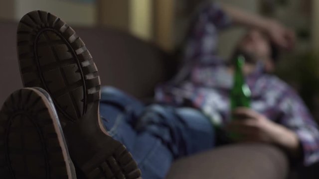 Drunk male sleeping on couch with bottle of beer in hand, bad news, emotions