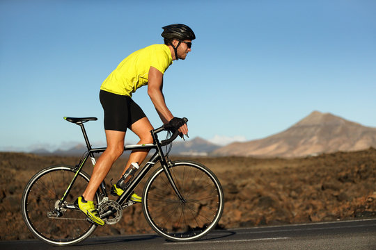 Biking cyclist male athlete going uphill on open road training hard on bicycle outdoors at sunset. Nature landscape.