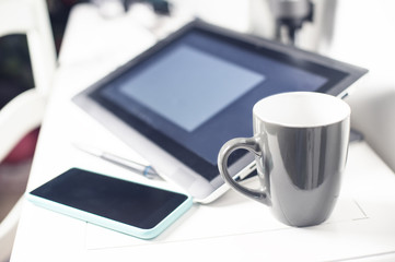 creative office white desk with graphic tablet, stylus, cell phone and a mug