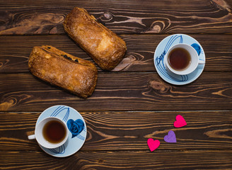 Cup of tea and a bun with raisins on a wooden table, top view. Space for text