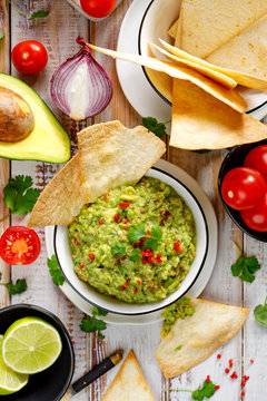 Guacamole,  traditional Mexican dip made of avocado, onion, tomatoes, coriander, chilli peppers, lime and salt with the addition of tortillas, top view. Vegetarian food