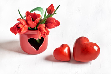 Two stone hearts and bunch of red tulips on white