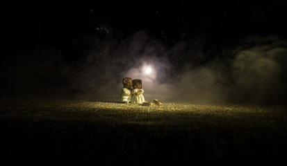 Fototapeta premium Stuffed bride and groom bears standing together with LED heart on dark foggy background.