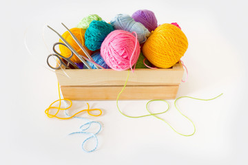 Colored yarn in the balls of a wooden box. Knitting needles and crochet hooks. Scissors. Isolate. White background.