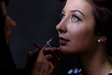 Obraz premium Makeup artist applies lips a red lipstick. Beautiful woman face. Perfect makeup on retro pinup or vintage pin up style