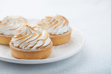 Lemon tartlets with meringue on vintage white plate on the stone table. Tasty treat on a light blue background. With copy space