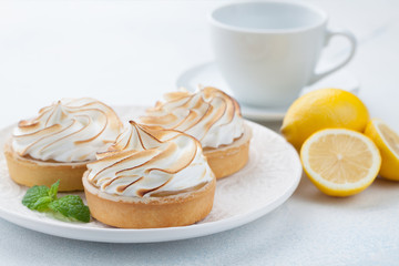 Lemon tartlets with meringue on vintage white plate and Cup of tea on the stone table. Tasty treat on a light blue background