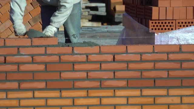 worker builds a wall of bricks. the builder on a building makes bricklaying. the builder at the construction site makes brickwork.
