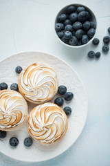 Delicious lemon tartlets with meringue on a white vintage plate. Sweet treat on a light blue background. Flat lay. Top view
