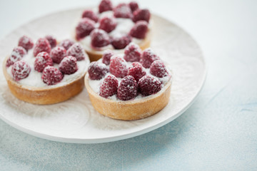 Delicious raspberry tartlets on a white vintage plate. Sweet treat on a light blue background