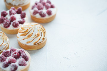 Delicious lemon and raspberry tartlets with meringue on a white vintage plate. Sweet treat on a light blue background. copy space