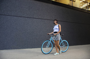 Full size portrait of attractive hipster woman walking with bicycle next to modern building 