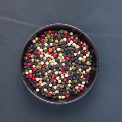 Four different kinds of peppercorns in clay bowl on stone background, top view, square