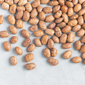 Uncooked dry pinto beans on gray concrete background, top view, square