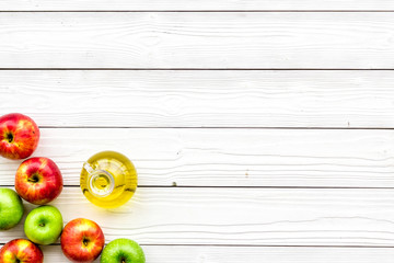 Apple cider vinegar in bottle among fresh apples on white wooden background top view copy space