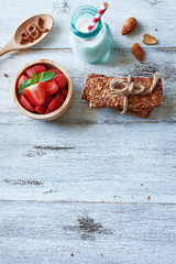 Top view of homemade muesli bars with almond milk and strawberry on white table with copy space.